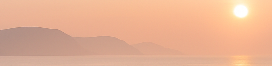 Sanfte Hügel am Wasser unter einem rosa-orangefarbenen Himmel mit Sonnenaufgang.