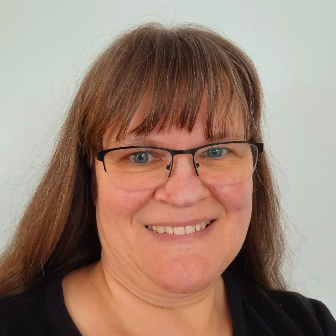 Eine lächelnde Frau, die Autorin Martina Klein mit langen, braunen Haaren und Brille vor einem hellen Hintergrund.